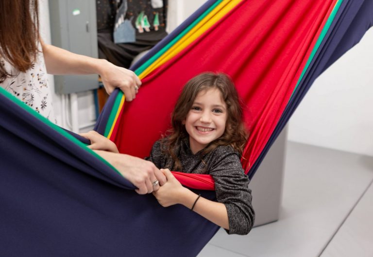 Child in a rainbow lycra hammock swing during sensory integration therapy